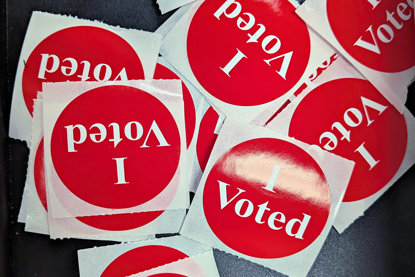 A scattered pile of round red stickers reading I Voted in white letters on a dark surface