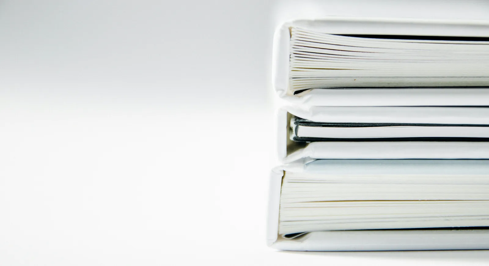 A stack of thick white binders on a white surface