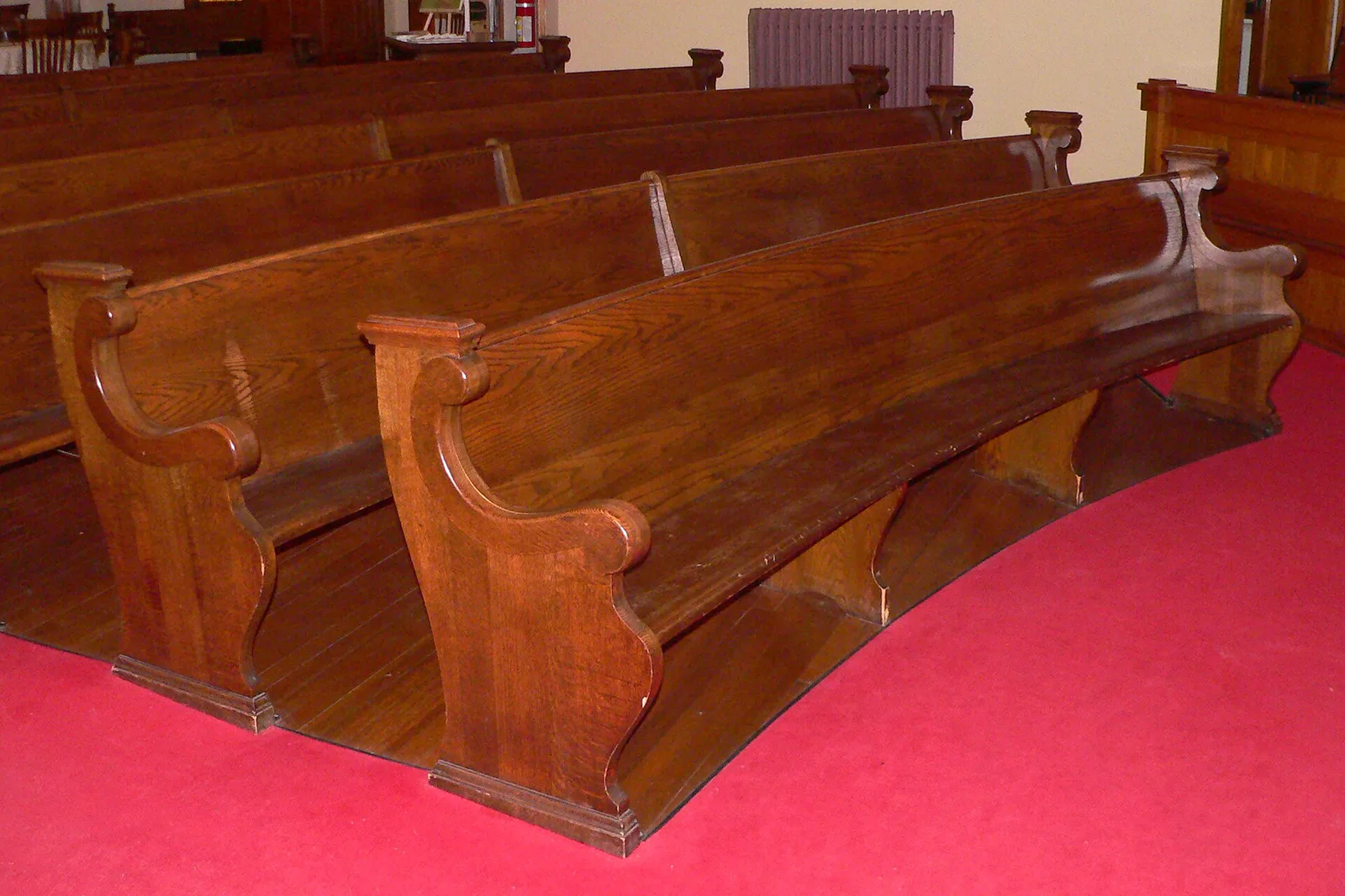 Rows of empty curved oak pews on a red carpet in a church sanctuary